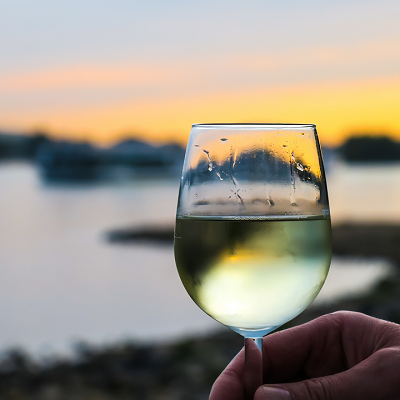 Hand holding white wine in a glass with water and sunset in background