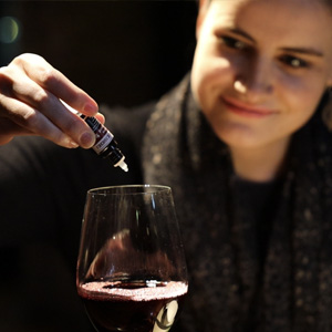 Girl putting wine drops into glass of red wine