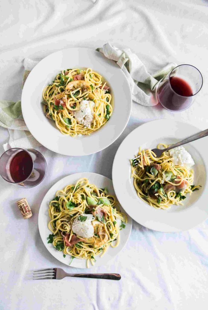 two stemless wine glasses with red wine and 3 plates of pasta