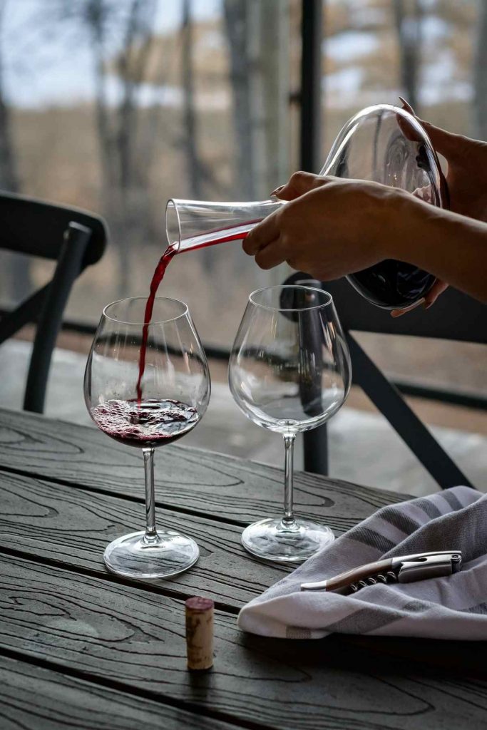 red wine in carafe being poured into wine glass sitting on table